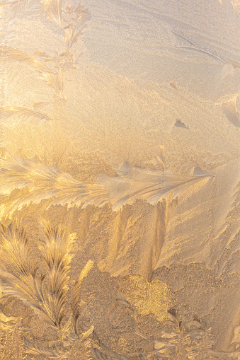 Evening sun and bright blue sky through the frost pattern on the window. Ice pattern and sunlight on winter glass.