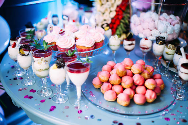 istock Beautifully decorated table with different cakes and sweets.Ice cream with jam and mint in glasses. Canapes with fruits. A large plate with pink bis. Jar with pink marshmallows. Palm with fruit. 1457663474