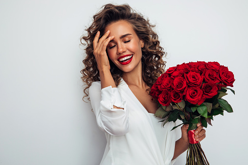 Beautiful red rose bouquet on woman hand, woman holding and showing red rose to camera while standing in decorative room. Romantic girl with flower for celebrating love on Valentine Day.