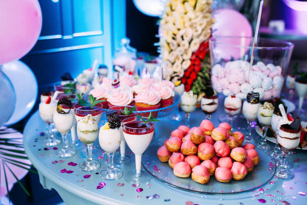 istock Beautifully decorated table with different cakes and sweets.Ice cream with jam and mint in glasses. Canapes with fruits. A large plate with pink bis. Jar with pink marshmallows. Palm with fruit. 1457663756
