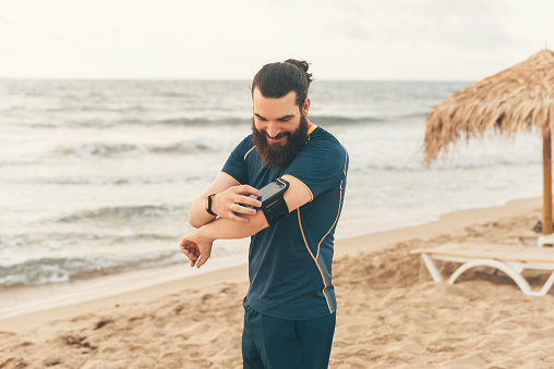 Photo of bearded runner using tracker on smart phone at beach