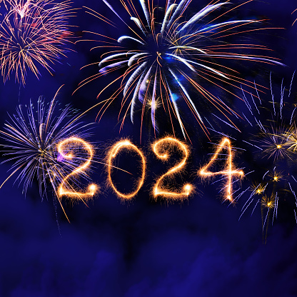 New Year fireworks and 2024 sign made of sparkler trace on a night blue sky background.