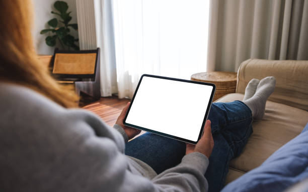 istock Mockup image of a woman holding digital tablet with blank desktop screen while lying on a sofa at home 1457666307