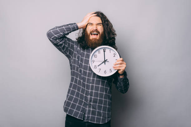 istock Handsome bearded young man holding big clock stressed and frustrated with hand on head, surprised and angry face 1457667661