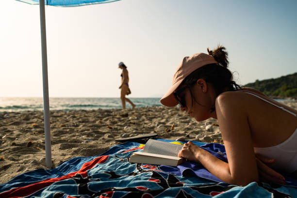 istock Woman on her summer vacations. Sunbathing on a sandy beach and reading a book 1457672525