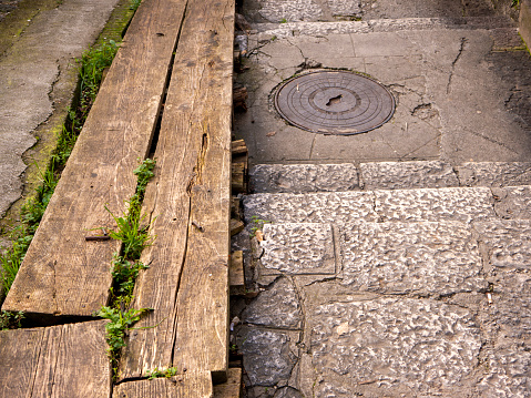 Ditch in asphalt footpath with stone steps covered with wooden boards