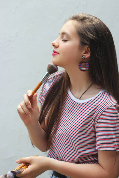 a young makeup artist girl holds a makeup brush, a teenager with makeup a young makeup artist girl holds a makeup brush, a teenager with makeup teenage girl before and after make up stock pictures, royalty-free photos & images