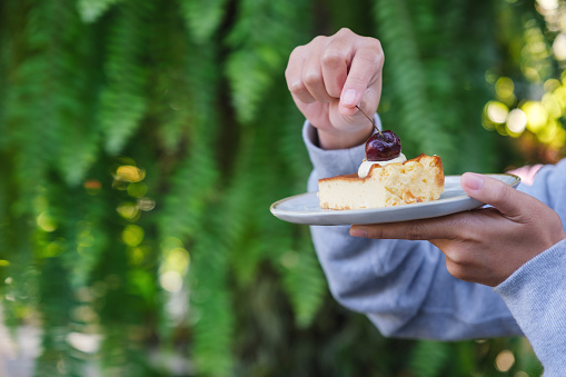 Closeup image of a woman holding and eating cheesecake with fork
