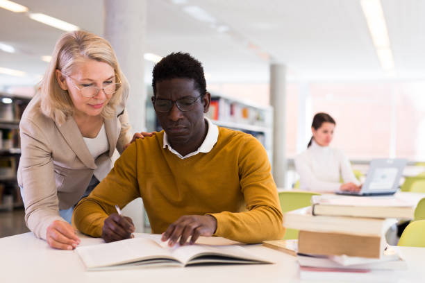 istock Friendly female tutor helping to diligent african-american man preparing for exam in library 1457675788