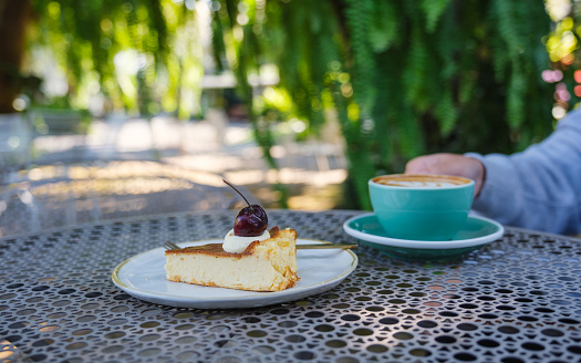 Closeup image of a woman drinking hot coffee with cheesecake on the table in the outdoors