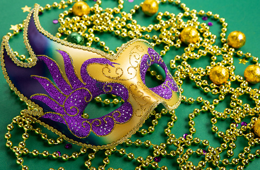 Mardi Gras masquerade festival carnival mask, gold beads and golden, green, purple confetti on green background. Holiday party invitation, greeting card concept.