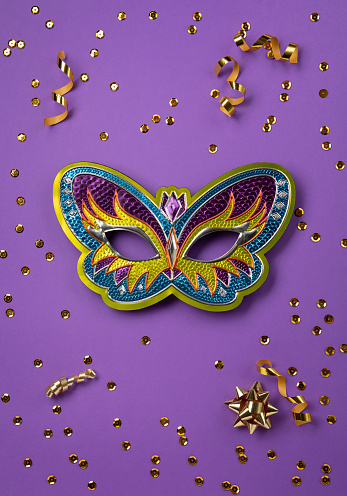 Mardi Gras masquerade festival carnival mask, gold beads and golden, green confetti on purple background. Holiday party invitation, greeting card concept.