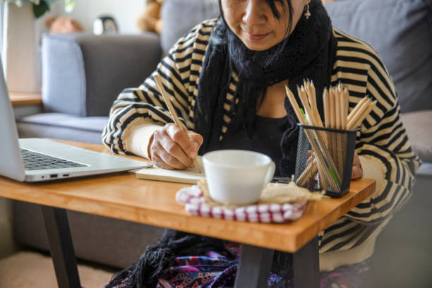 istock Working from home concept. Planner using phone and laptop to plan daily agenda on calendar book. Woman mark and noted schedule (holiday trip) on diary at home office desk. Coffee place on table 1457679093