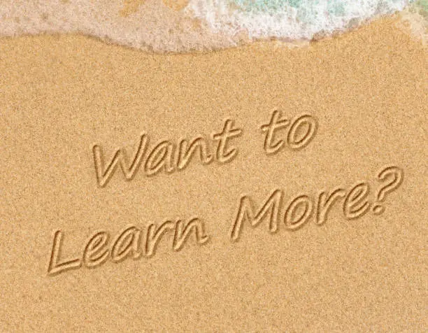 Want to Learn More? Sign on the sand on the beach with the sea washing up the shore