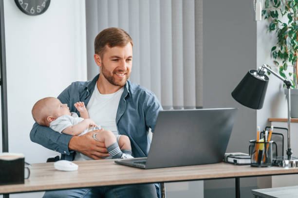 istock Working by using laptop. Holding baby. Father with toddler is indoors in the office 1457681663