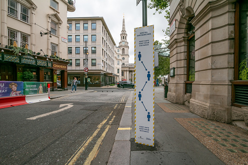 Social Distancing Sign near Trafalgar Square in City of Westminster, London, with people visible in the background.