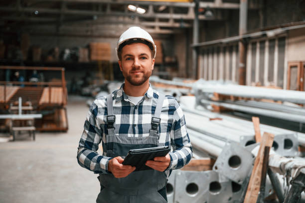 istock Factory male worker in uniform is indoors. Standing, holding tablet 1457683568