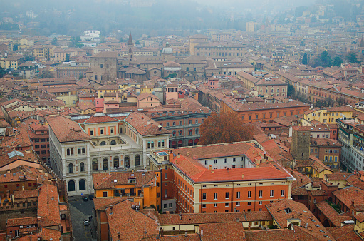 Mysterious foggy high perspective view from the tower on Bologna old town center. Old buildings with red tile roofs. Famous touristic place and travel destination in Europe.UNESCO World Heritage Site.