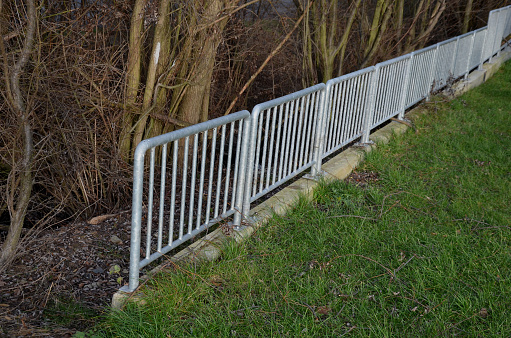 railing at the bridge with vertical fence bars anchored to the ground with four concrete screws. plastic caps, lawn park  stream, simple, pole, pipe, handrail