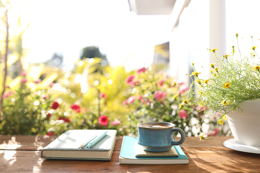 Coffee cup and notebook and daisy flower on wooden table outdoor