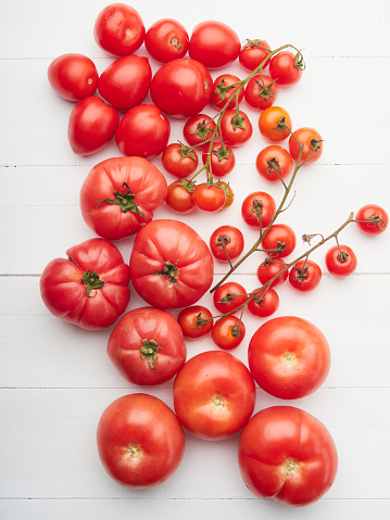 varieties of red organic tomatoes on a white wood surface, top view