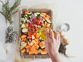 female hand with bottle of olive oil seasoning vegetables on baking tray