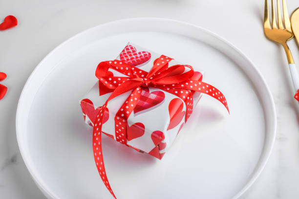 istock Valentines day dinner background with gift with red hearts on white plate with fork and knife on white marble, close up 1457690593