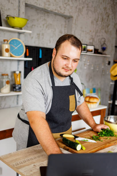 istock Overweight man using laptop while prepares healthy meal in the kitchen 1457690997