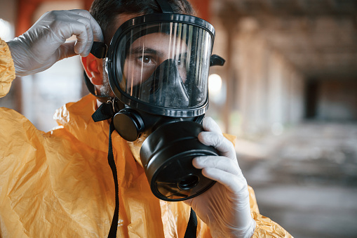 Wearing the respirator. Man dressed in chemical protection suit in the ruins of the post apocalyptic building.