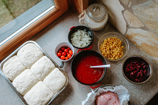 Raw dough for pizza with ingredient: tomato sauce, dough, mozzarella, tomatoes, basil, olive oil, corn, cherry tomatos, onion, beens, ham