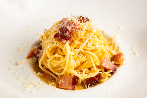 Delicious looking carbonara pasta with some parmesan and bacon in a white plate.