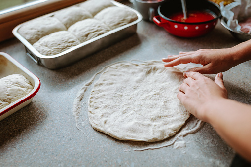 Woman preparing pizza at home, spreding the dough