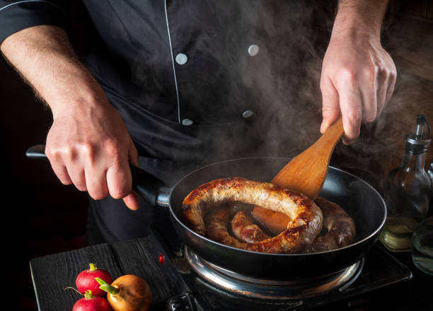 cooking meat sausage in the restaurant kitchen. the chef fries sausage in frying pan. the idea of a delicious meat dish - sausage food mash grilled imagens e fotografias de stock