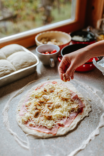 Woman making original italian pizza at home, putting mushrooms on pizza