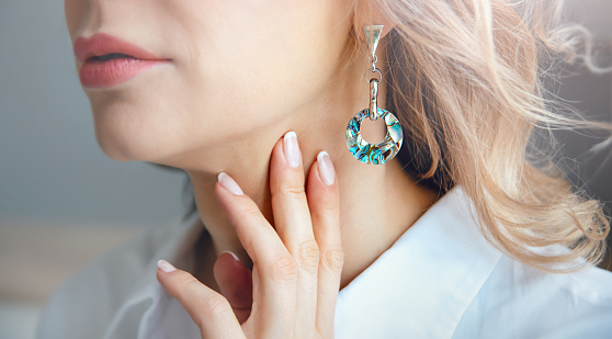 Women's jewelry. Close-up of a mother-of-pearl earring on a woman's ear. Hand with a beautiful French manicure.