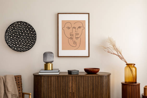istock The creative composition of living room interior with mock up poster frame, wooden commode, armchair, plaid, black books, glass lamp, vase with dried flowers and personal accessories. Home decor. Template. 1457704287