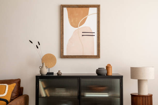 istock Creative composition of living room interior with mock up poster frame, black commode, lamp on the wooden stand, vase with dried flowers, candle and elegant personal accessories. Home decor. Template. 1457704372