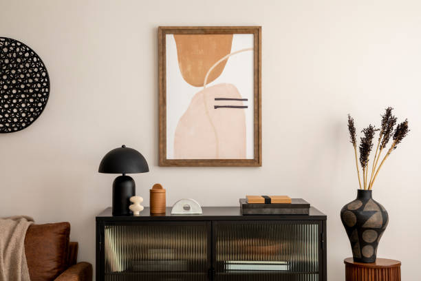 istock Creative composition of living room interior with mock up poster frame, black commode, vase with dried flowers on the wooden stand, books, lamp and stylish personal accessories. Home decor. Template. 1457704392
