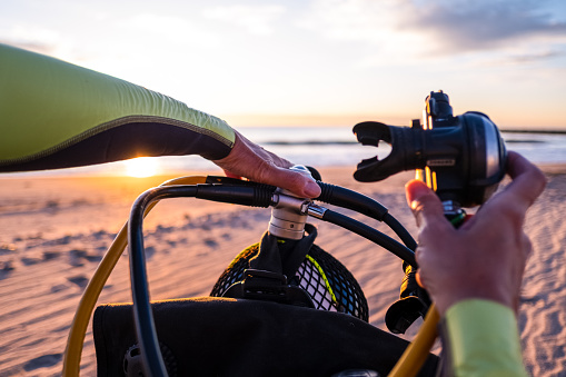 Hands of a person preparing scuba diving equipment on a beach at dawn. Point of view.