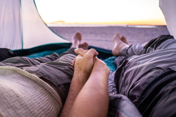 um casal de mãos dadas observa o nascer do sol em uma praia tranquila de dentro de uma tenda. ponto de vista. - sunrise beach couple hiking - fotografias e filmes do acervo