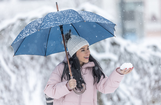 Happy woman holding an umbrella on a cold snowy day and holding fresh snow in her hand.