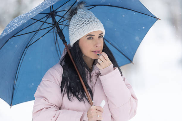 Gorgeous brunette puts on lip balm dressed in warm clothes outdoors on a cold winter day.