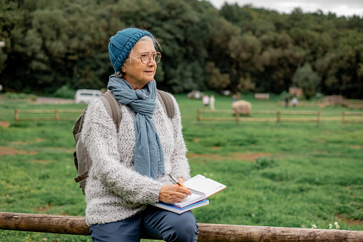 An attractive older Caucasian woman on a hike makes notes on a pad feeling inspired by the beauty of nature. Active senior woman on a leisure trip admiring the scenery