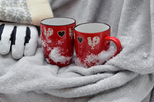 two red mugs with heart shaped on a plaid with snow and gloves and hat background