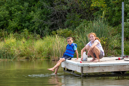 Young boy and his older sister fishing from a wooden dock at the lake on a beautiful late summer/early autumn evening.
