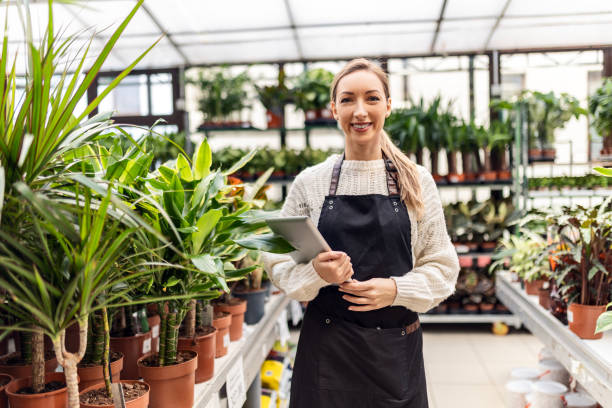 istock Young florist working in greenhouse looking at camera holding digital tablet 1457713314