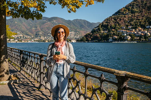 Beautiful young woman using smart phone at the Lake Como in Como, Italy.