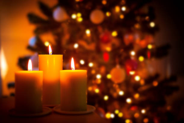 Christmas burning candles on garland lights blurred background, selective focus, decorative New Year 2023 card with copy space