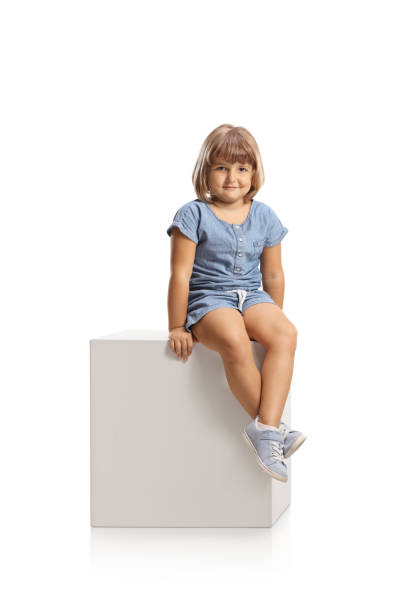 istock Cute little girl sitting on a white cube and smiling 1457718824
