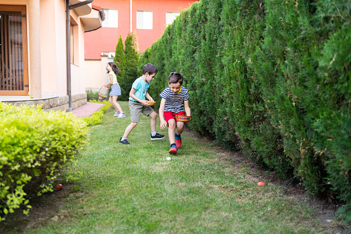 Three children are searching in a garden looking for the hidden Easter eggs outside on a sunny day